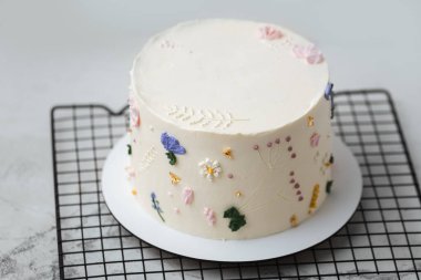 Gri pastel arka planda krema çiçekleriyle süslenmiş beyaz çikolata kremalı güzel bir doğum günü pastası.