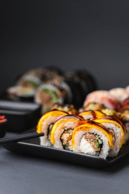 Somon, avokado ve ton balıklı suşi. Suşi seti siyah arkaplanda siyah çubuklu kırmızı zencefilin yanında servis edilir.