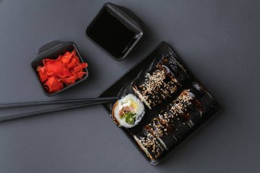 Suşi, somon, avokado ve yosunla sarılmış ton balığı. Suşi seti siyah arka planda siyah çubuklu kırmızı zencefilin yanındaki siyah tabakta servis ediliyor. Düz yatıyordu