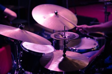 Close-up of a drum kit being played during a jazz performance, with emphasis on the cymbals and drumsticks under stage lighting. Selective focus. clipart