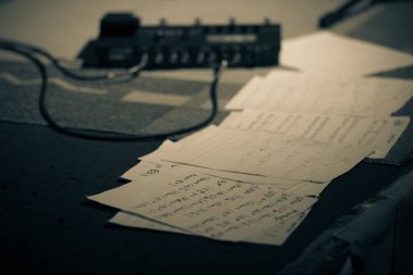 Bir caz performansı sırasında sahnede, arka planda elektrik pedalı olan bir nota kağıdının yakın çekimi. Sahne, canlı performansın hazırlık ve detaylarını yakalıyor..