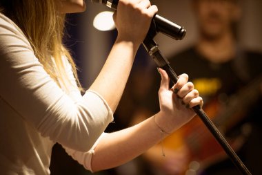 Elinde mikrofon olan bir şarkıcıya yakın çekim, performansın ortasında kaydedilmiş. Ilık ışıklandırma performansın yoğunluğunu vurgular.