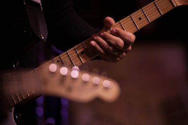Arka planda bulanık başka bir gitarla gitar çalan bir elin yakın çekimi. Tellere ve panoya odaklan..