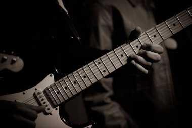 Canlı bir gösteri sırasında elektro gitar çalan gitarist elleri ve gitar boynuna odaklanmış siyah beyaz bir şekilde yakalandı..