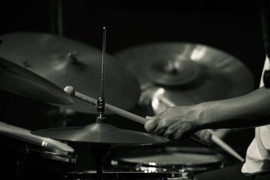 Black and white close-up of a drummer's hands playing cymbals during a live performance, focusing on the motion and rhythm.