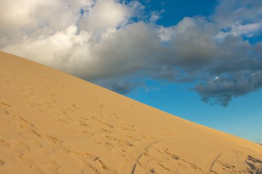 Parlak mavi gökyüzüne karşı dik bir kum tepesinde yürüyen yalnız bir figür. Fotoğraf, çöl manzarasının sonsuzluğunu ve yalnızlığını yansıtıyor. Jericoacoara, Brezilya.