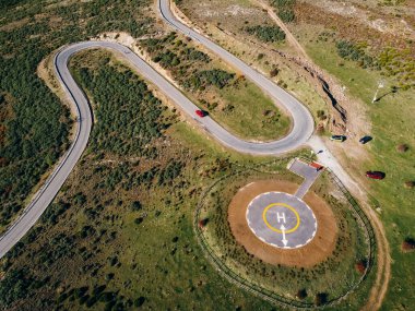 Virajlı yolun havadan görünüşü. Asfalt yolda muhteşem bir sabah manzarası. Helikopterler için helikopter pisti. Helikopter inişleri için helikopter pistinin havadan görüntüsü. Seyahat konsepti arka planı.