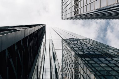 Londra şehrindeki modern ofis binalarının alçak açılı görüntüsü ve perde önü yansımaları. Kopyalamak için beyaz bulutlu mavi gökyüzüne karşı görüntüle