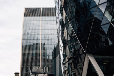 Londra, İngiltere - 25 Ağustos 2023: Londra 'daki modern ofis binalarının düşük açılı görüntüsü ve perde önü yansımaları. Beyaz bulutlu mavi gökyüzüne bak