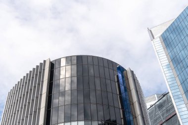 Londra, İngiltere - 25 Ağustos 2023: Londra 'daki modern ofis binalarının düşük açılı görüntüsü ve perde önü yansımaları. Kopyalamak için beyaz bulutlu mavi gökyüzüne karşı görüntüle