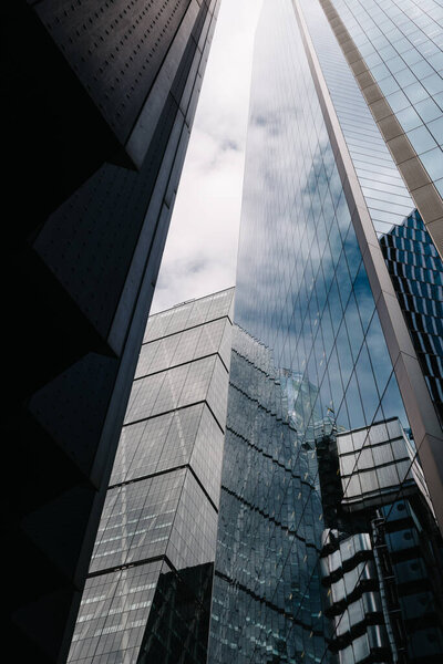 London, UK - August 25, 2023: Low angle view of modern office buildings in the City of London and reflections on curtain wall facade. View against blue sky with white clouds. Business concept