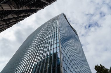 Londra, İngiltere - 25 Ağustos 2023: Londra 'daki modern ofis binalarının düşük açılı görüntüsü ve perde önü yansımaları. Kopyalamak için beyaz bulutlu mavi gökyüzüne karşı görüntüle