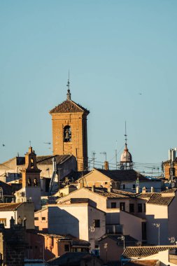 Parlak, güneşli bir günde, açık mavi gökyüzünün altında bir çan kulesinin ve büyüleyici çatıların bulunduğu pitoresk bir şehir manzarası. Toledo.