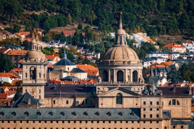 A landscape view of the Royal Monastery of San Lorenzo de El Escorial in Spain, showcasing its architectural grandeur against a backdrop of town and nature. clipart