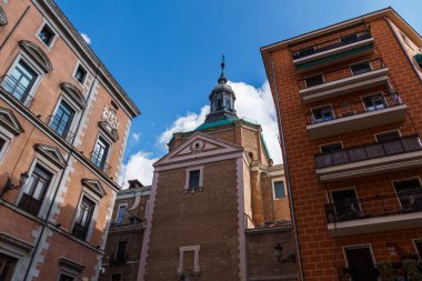 Düşük açılı bir çekim Madrid 'in mimari ahengini yansıtıyor. Yerleşim yerlerinin ortasında parlak mavi gökyüzüne karşı tarihi bir kilise sergiliyor..