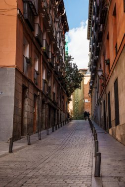 Madrid, İspanya - 2025-02-22: Dar bir kaldırım taşı caddesi Madrid 'deki tarihi binalar arasında yavaşça yükseliyor, güneşli bir günde büyüleyici bir şehir manzarası yaratıyor.