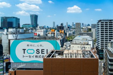 Tokyo, Japonya - 4 Ağustos 2024: Tokyo, Japonya 'nın canlı Shibuya ilçesinin göz seviyesindeki manzarası, mavi gökyüzü altında modern ve eski binaların bir karışımını gösteriyor.