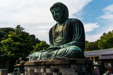 Kamakura, Japonya - 5 Ağustos 2024: Serin bronz Büyük Buda heykeli, yemyeşil ve mavi gökyüzü ile çevrili Japonya 'nın Kamakura kentinde huzur içinde duruyor.