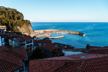 Teknelerle dolu sakin bir limana bakan bir yamaçta yuva yapmış güzel bir sahil kasabası. Sahne güneş ışığıyla yıkanmıştı. Lastres, Asturias