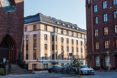 Helsinki, Finlandiya - 19 Ağustos 2024: Helsinki 'de sokak manzarası açık bir günde tuğla binalar, kilise, bisikletler ve park halindeki arabaları gösteriyor.
