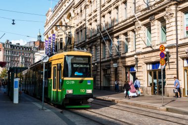 Helsinki, Finlandiya - 19 Ağustos 2024: Helsinki, Finlandiya 'da yeşil ve sarı bir tramvay, yaya geçitleri ve arka planda tarihi binalar bulunan bir cadde boyunca seyahat etmektedir..