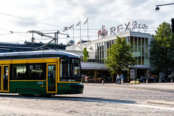 Helsinki, Finlandiya - 19 Ağustos 2024: Helsinki, Finlandiya 'da bir sokak manzarasında, tarihi Rex Bio sinemasının önünden parlak bir günde geçen yeşil ve sarı bir tramvay görülüyor.