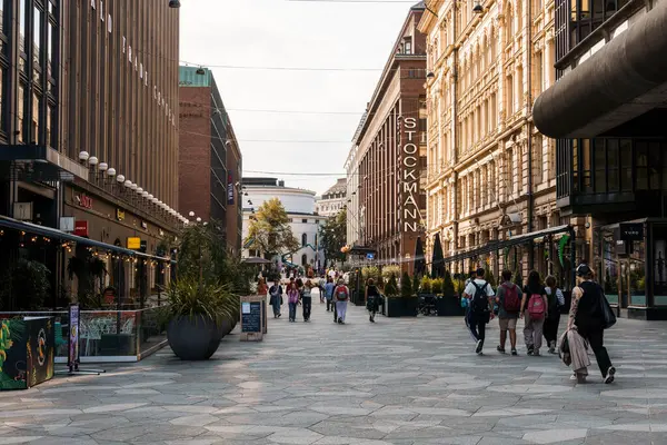 Helsinki, Finlandiya - 19 Ağustos 2024: Halk, Finlandiya 'nın Helsinki kentindeki Stockmann mağazası da dahil olmak üzere klasik binalar tarafından çerçevelenmiş yaya caddesi boyunca yürüyor.