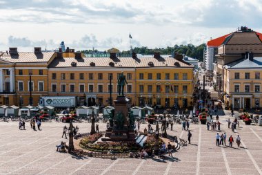 Helsinki, Finlandiya - 19 Ağustos 2024: Senato Meydanı, Helsinki, gündüz vakti bulutlu bir gökyüzü altında heykel ve market tezgahları etrafında yürüyen insanlar.