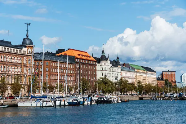 Helsinki, Finlandiya - 19 Ağustos 2024: Parçalı bulutlu bir gökyüzü altında renkli binalar ve yelkenlilerin yer aldığı Finlandiya 'nın Helsinki kenli liman manzarası.