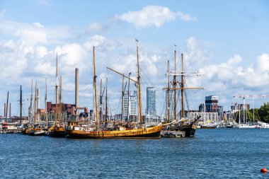 Helsinki, Finlandiya - 19 Ağustos 2024: Güneşli bir günde arka planda sanayi ve konut binaları bulunan Finlandiya 'nın Helsinki kentindeki limanlı yelkenli koleksiyonu.