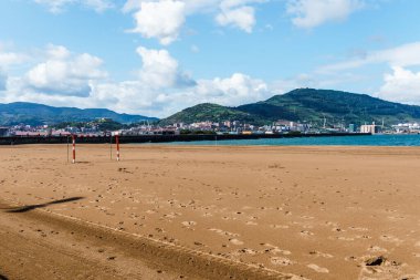 Açık ve güneşli bir günde Getxo 'da arkası dağlarla kaplı kumlu bir sahil manzarası..