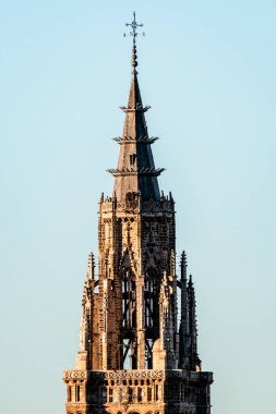 Toledo Katedrali 'nin çan kulesinin çarpıcı bir görüntüsü gün batımında açık mavi gökyüzüne karşı karmaşık Gotik mimarisini sergiliyor..