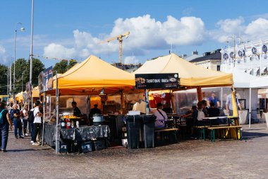 Helsinki, Finlandiya - 19 Ağustos 2024: Helsinki, Finlandiya 'da açık hava gıda pazarı, insanların güneşli gökyüzü altında gezinip yemek yediği geleneksel Fin mutfağını gözler önüne seriyor.