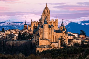 İspanya 'daki karlı Guadarrama dağlarına karşı Segovia ikonik Alcazar ve Katedral' in panoramik manzarası. Gün batımında görüntüle
