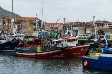 Santona, İspanya - 1 Mayıs 2025: Santona Limanı, Cantabria, İspanya 'da bulutlu bir gökyüzü altında bulunan balıkçı teknelerini yakalayan canlı bir çekim.