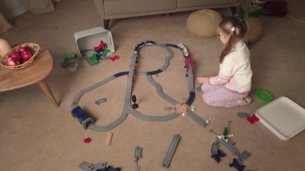 Счастливая Маленькая Девочка Строит Игрушечную Пластиковую Железную Дорогу Играет Поездом — стоковое видео