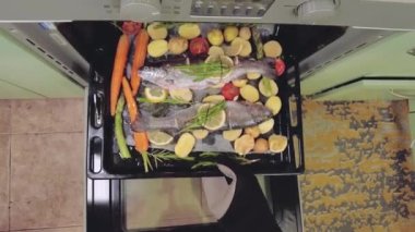 Izgarada pişirmek için deniz levreği balığı hazırlıyorum. Aromatik otlar ve sebzeler koyu renkli tepsi tepsisinde.