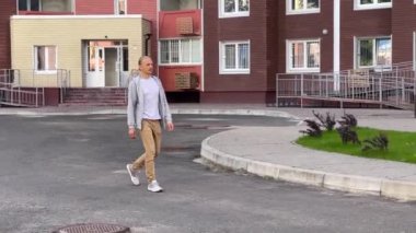 Genç bir birey, arka planda modern binaların yer aldığı sakin bir şehir parkında geziniyor.