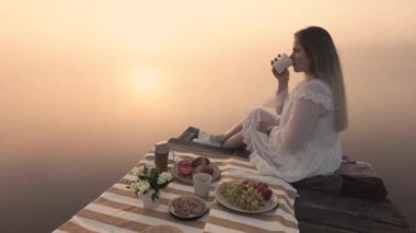 Kadınlar kahve içer ve güneşin doğuşundaki sisli gölün ve doğanın tadını çıkarırlar.