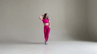 Tarafsız gri bir duvara karşı canlı pembe bir kostümle salsa yapan bir kadın. Dans, hareket, performans ve sanatsal ifade için mükemmel.