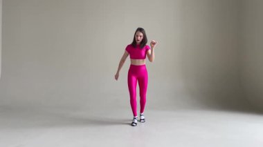 Tarafsız gri bir duvara karşı canlı pembe bir kostümle salsa yapan bir kadın. Dans, hareket, performans ve sanatsal ifade için mükemmel.