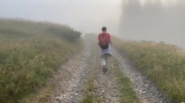 Sisli dağ yolunda tek başına yürüyüş yapan bir kadın. Doğanın nefes kesici ve çarpıcı manzaralarıyla çevrili.