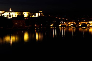 Prag ve Charles köprüsü gece Vltava nehrinde ışık yansımalarıyla