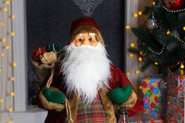 Noel Baba hediye dolu büyük bir çanta taşıyor, Noel ağacının yanında.