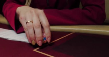 Kırmızı masada elinde fiş ve kartlarla poker oynayan kadın. Eline odaklan.
