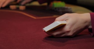 Kırmızı masada elinde fiş ve kartlarla poker oynayan kadın. Eline odaklan.