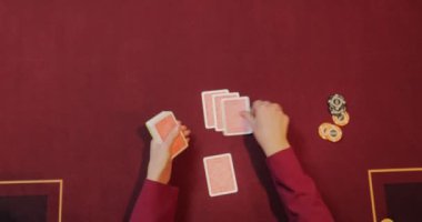 Kırmızı masada elinde fiş ve kartlarla poker oynayan kadın. Eline odaklan.