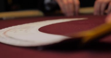 Kırmızı masada çiplerle poker oynayan ellerin yakın çekimi.
