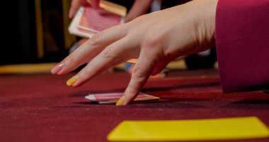 Kırmızı masada çiplerle poker oynayan ellerin yakın çekimi.