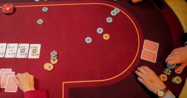 Kırmızı masada çiplerle poker oynayan ellerin yakın çekimi.